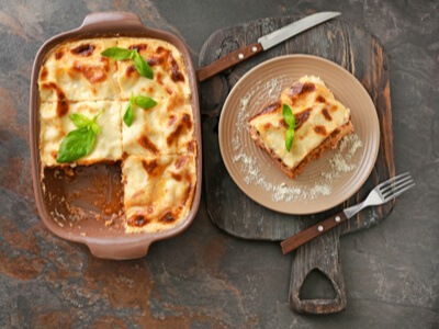 Lasagna casserole with a plate of lasagna on a natural wood table